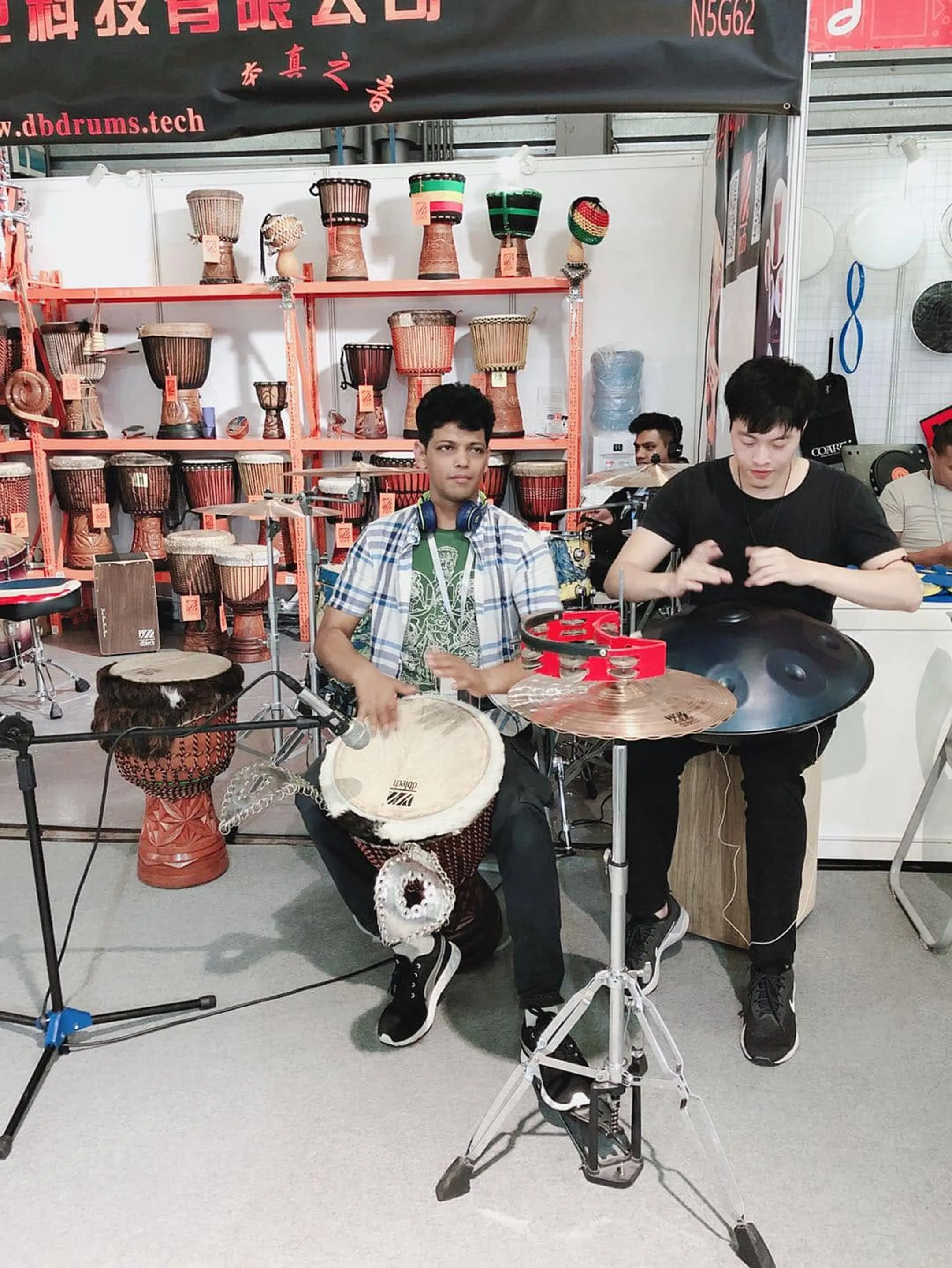 A DBTECH stand at a trade fair, hand drums and cymbals on display.